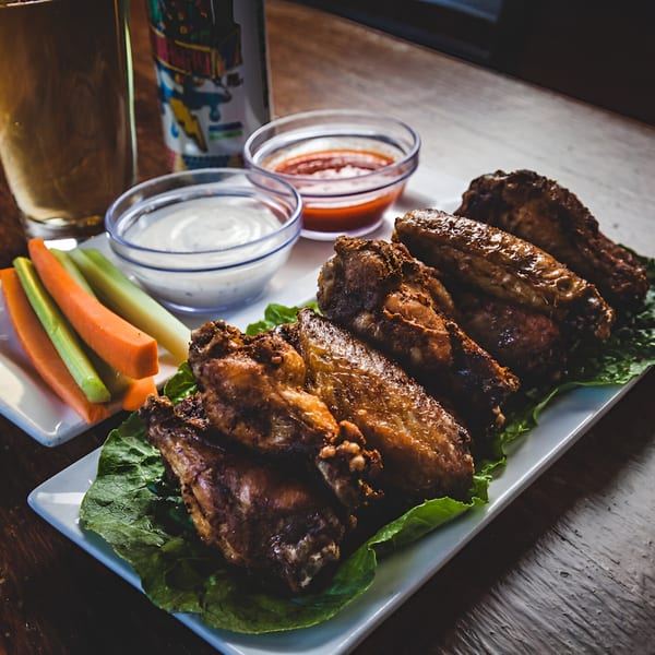 A plate of La Porchetta Kitchen's chicken wings with dipping sauces, carrots, and celery.