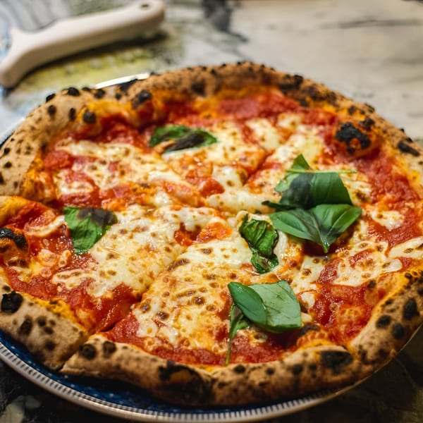 A freshly baked La Porchetta Kitchen pizza, topped with melted cheese, tomato sauce, and basil leaves.