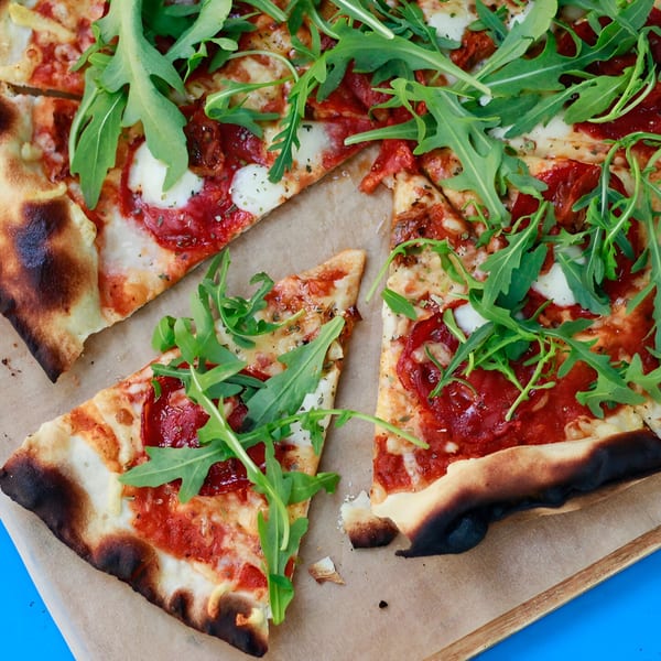 La Porchetta Kitchen pizza with tomato sauce, mozzarella, and fresh arugula on a wooden board.