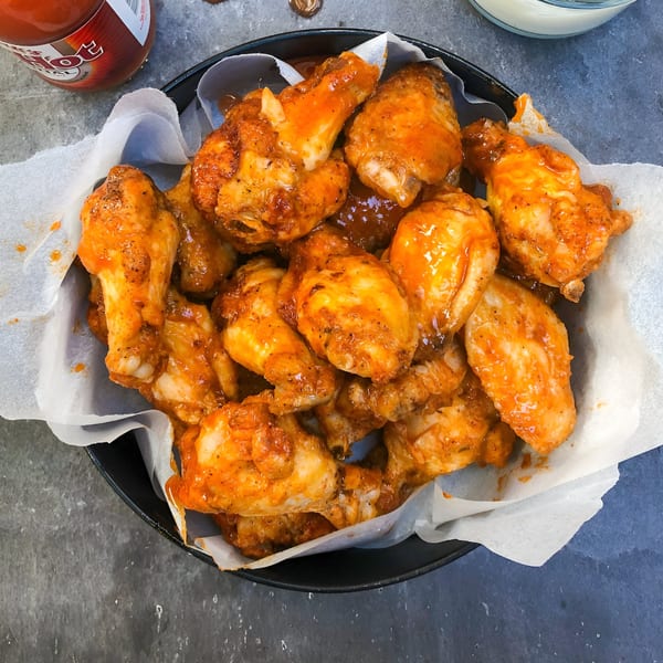 A black bowl filled with La Porchetta Kitchen's buffalo chicken wings, with hot sauce and dip.