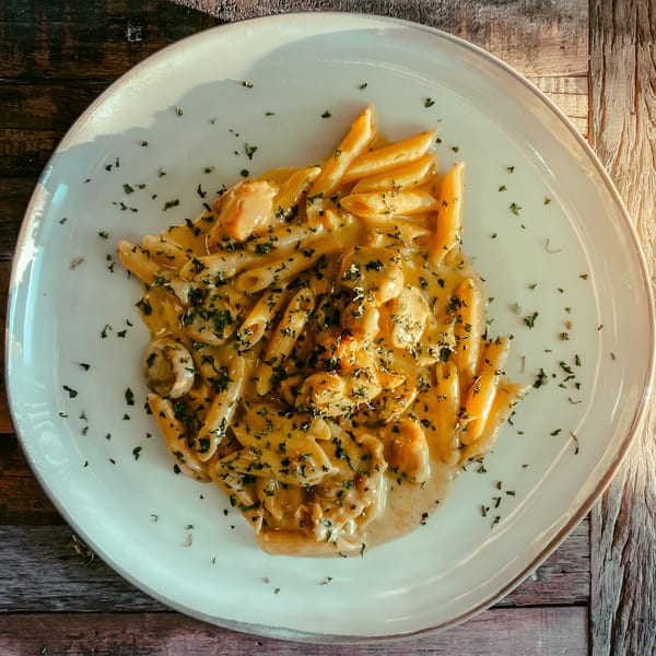 Creamy penne pasta with chicken and mushrooms, garnished with herbs on a white plate.